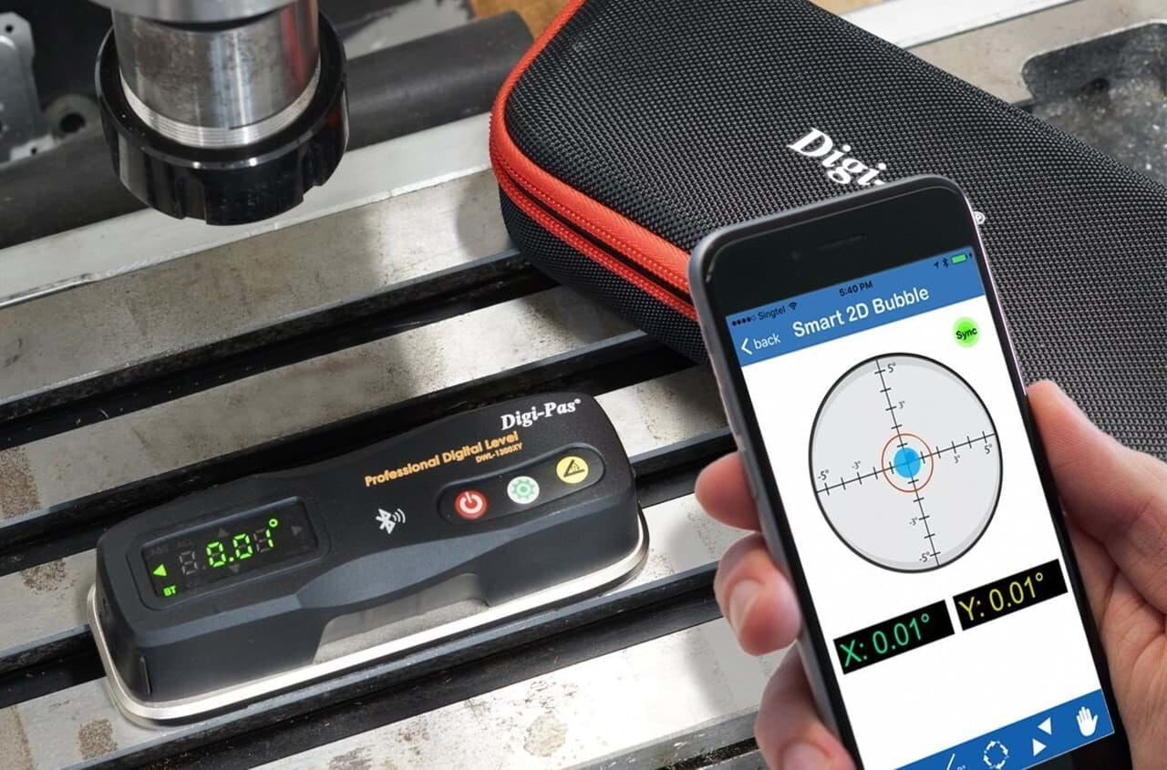 Eine Digi-Pas Präzisionswasserwaage im Einsatz. Das Gerät liegt auf einer Werkbank, daneben das Etui. Im Vordergrund hält eine Hand ein Handy auf dem man die Digi-Pas Software sehen kann.