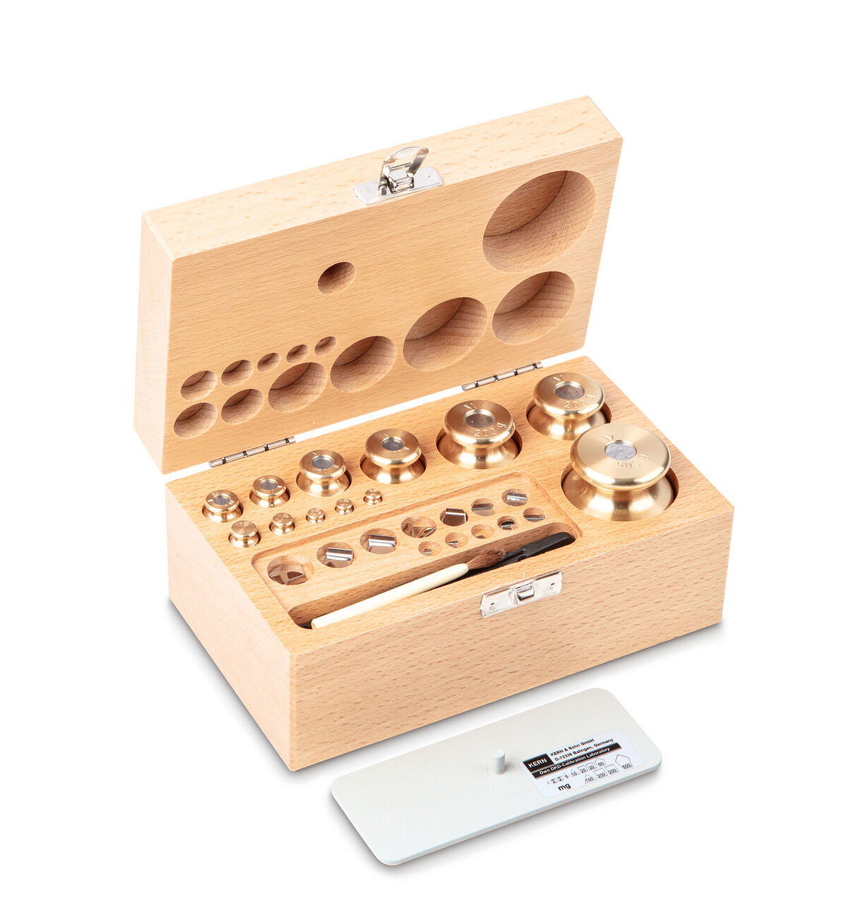 Holzkoffer auf weißem Hintergrund. Ein kompletter Gewichtssatz und ein Pinsel sind im Inneren zu sehen. Davor liegt eine kleinere weiße Schale.