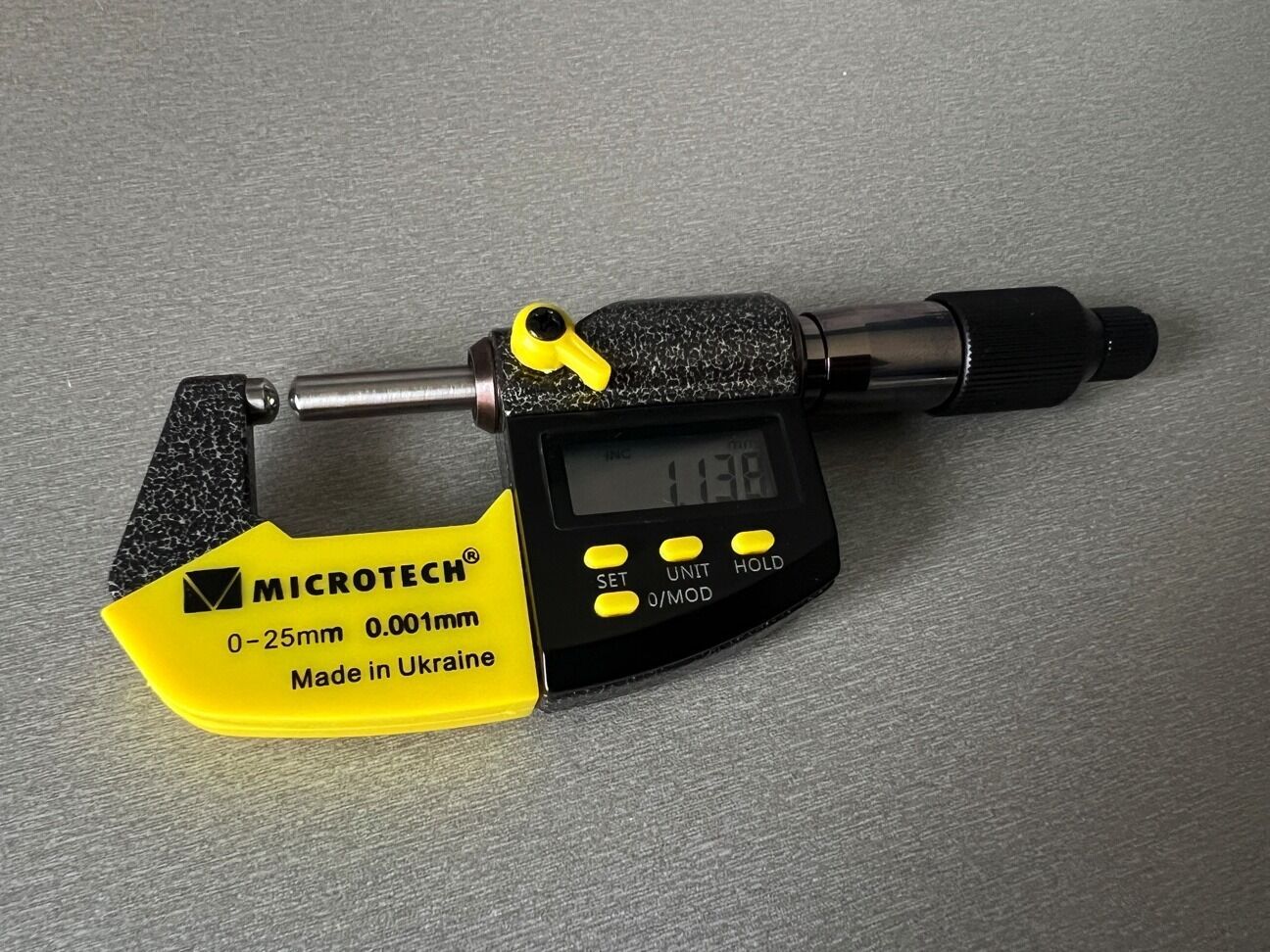 Microtech Digital Messschraube: Gelb-schwarzes Aluminiumgehäuse, Frontalansicht auf grauem Untergrund