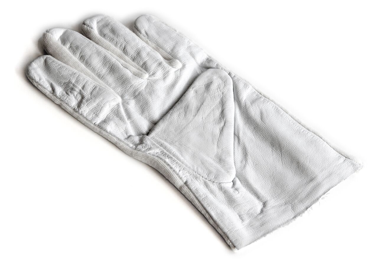 Weißer Lederhanschuh auf weißem Hintergrund. Der Handschuh liegt flach auf einer Oberfläche, der Dauem ist dabei auf der Handfläche gefaltet.