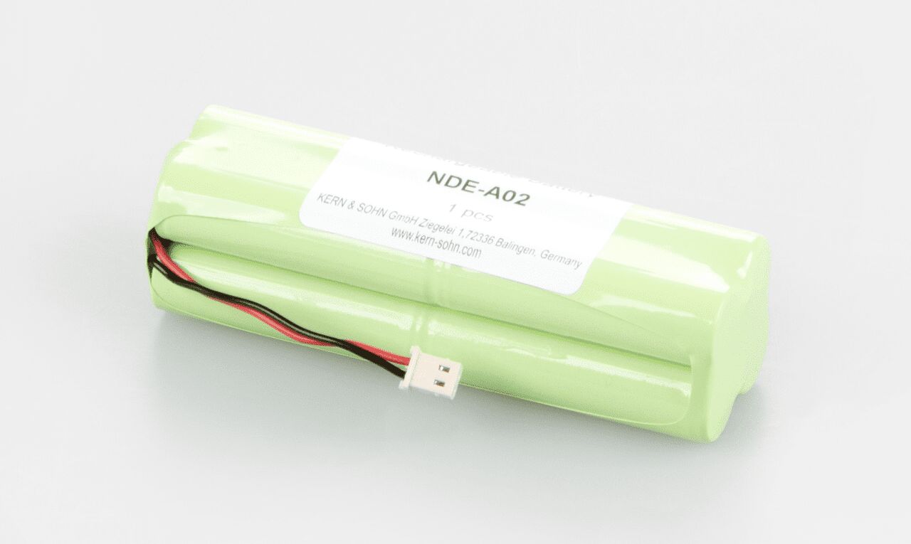 Akkubetrieb zum Einbauen in die Waage auf weißem Hintergrund. Der Akkubetrieb besteht aus mehreren zusammengeschweißten Batterien. Die Außenhülle ist hellgrün, oben klebt eine Etikette mit der Artikelnummer. Aus der Seite ragt ein Kabel.