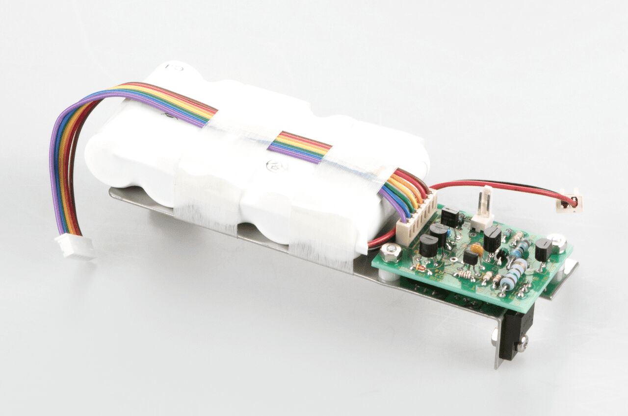Akkubetrieb auf weißem Hintergrund. Der Akkubetrieb besteht aus einem motherboard und mehreren in weißer Plastik eingeschweißten Batterien. Mehrere bunte Kabel strecken sich über die Batterien aus.